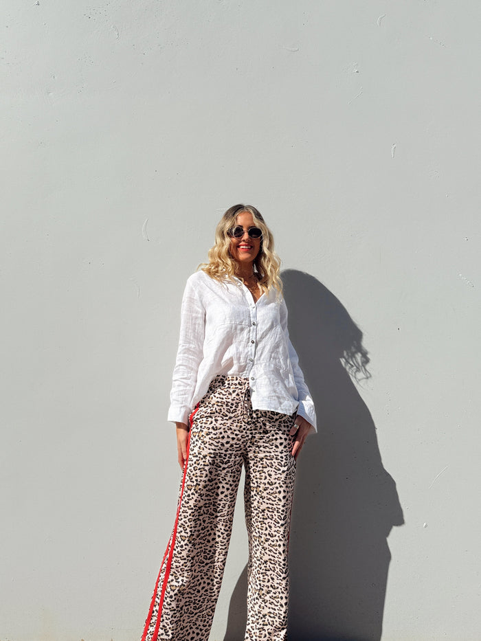 Lady wearing a white shirt and leopard print pants against a light gray wall.