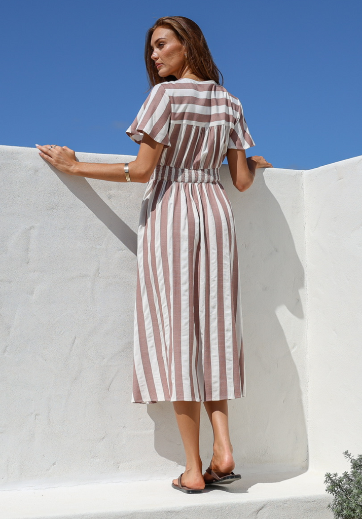 Woman wearing a striped dress against a white wall with blue sky.